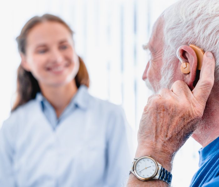 Focused picture of an elderly male patient with hearing aid side view with blurred woman